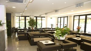 A modern hotel lobby with multiple seating areas, large windows, and potted plants. - Hotel Ambra (Cesenatico)