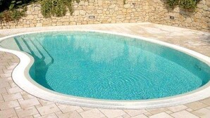 Una piscina de borde curvo, rodeada por un muro de piedra y un sendero de ladrillo.