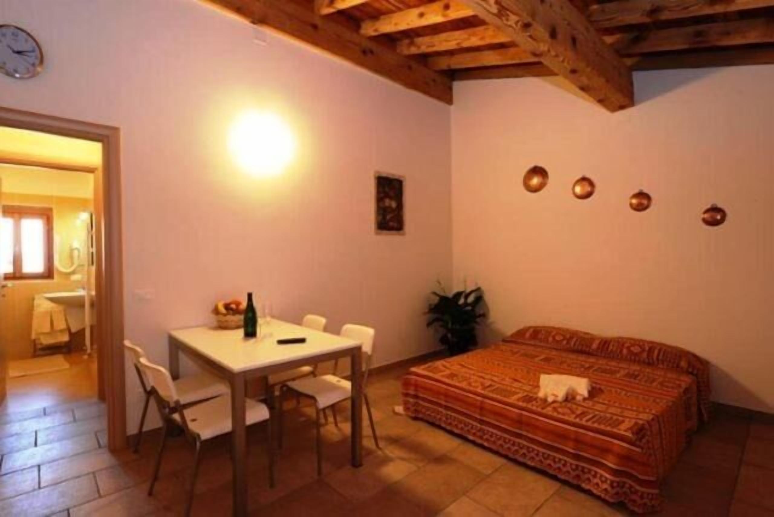 Una habitación con cama, una mesa con sillas, un reloj en la pared y una puerta que da a otra estancia.