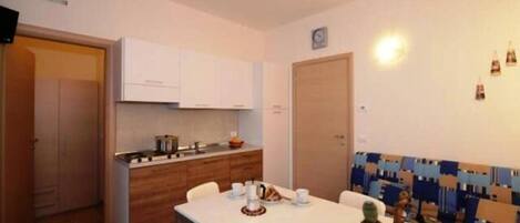 A compact kitchen with white cabinets, a dining table with chairs, and a patterned sofa.