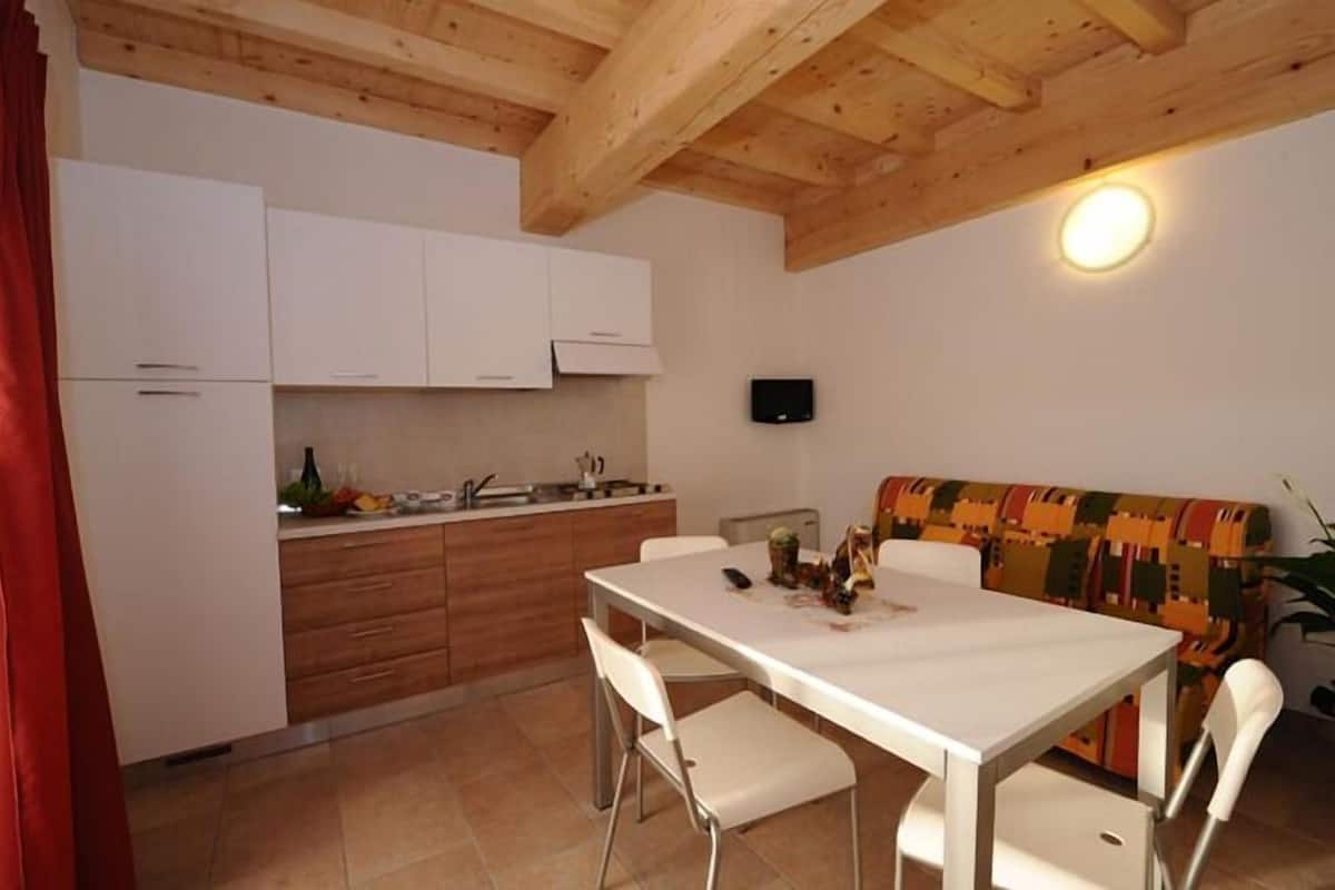 A compact kitchen with white cabinets, a dining table with chairs, and a colorful sofa.