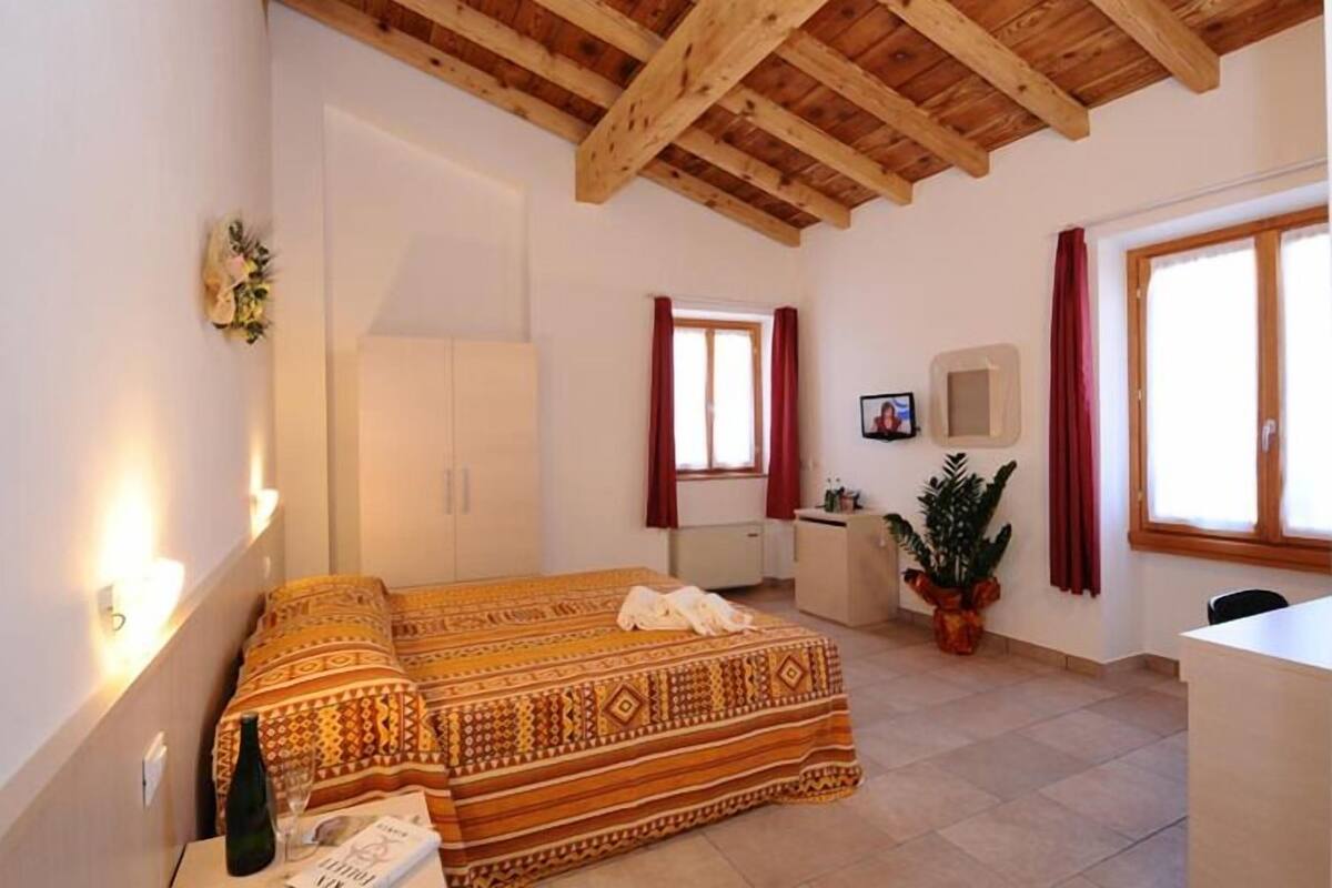 A bedroom with a bed, a desk, a chair, a potted plant, and a window with curtains.