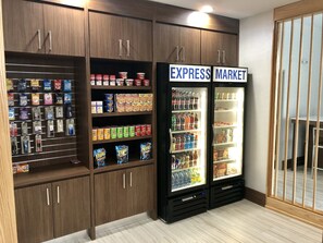 Uma loja com prateleiras repletas de lanches e bebidas, e dois refrigeradores com a inscrição 'EXPRESS MARKET'.