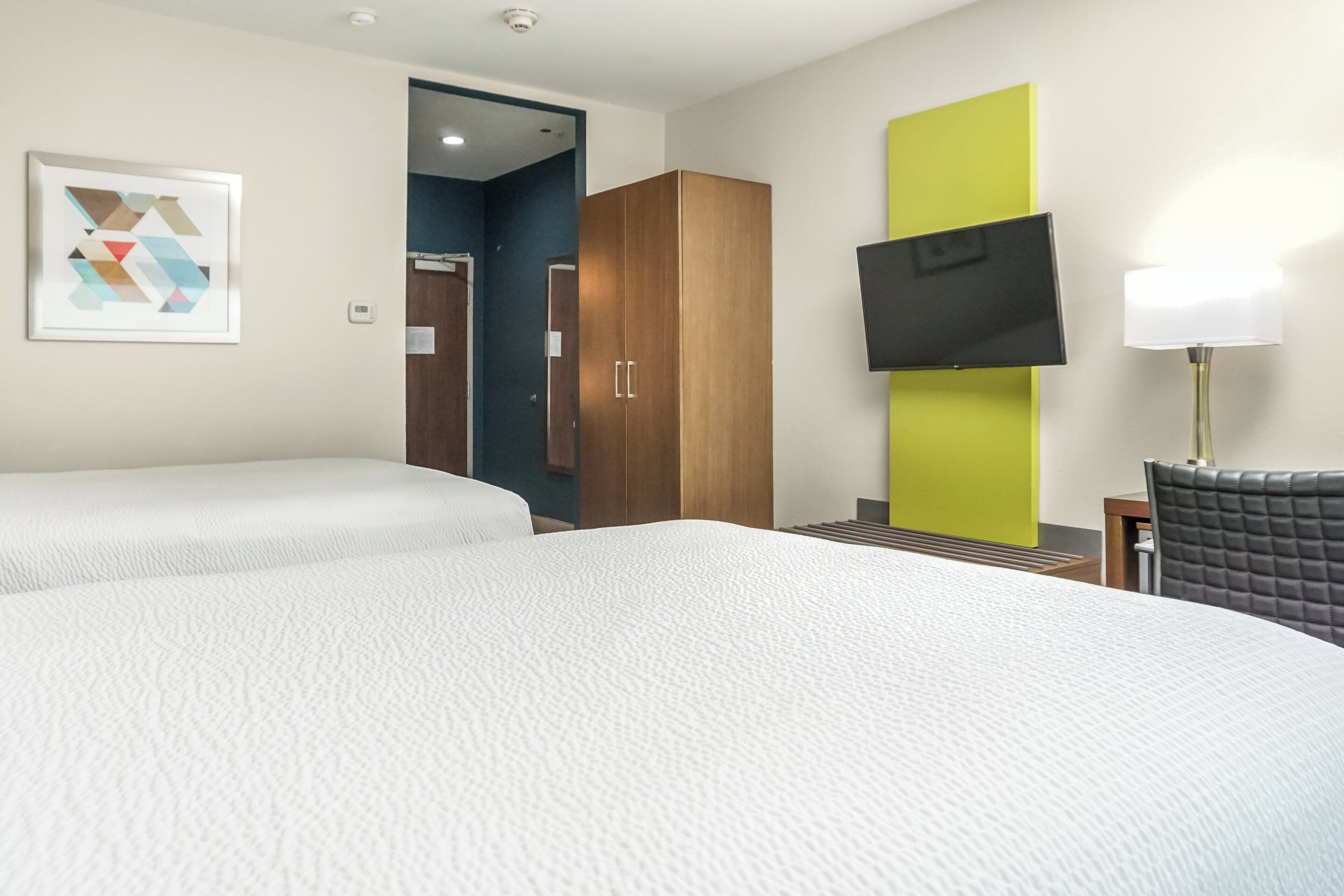 A hotel room with two beds, a wardrobe, a television, and a lamp.