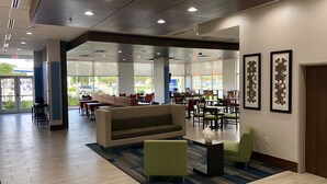 A spacious indoor area with a seating arrangement, including a sofa and chairs, and a large window providing a view of the outside. - Holiday Inn Express and Suites Houston Westchase - Westheimer by IHG (Houston)