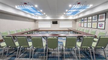 A conference room with a long table, green chairs, white screens, and patterned carpet.