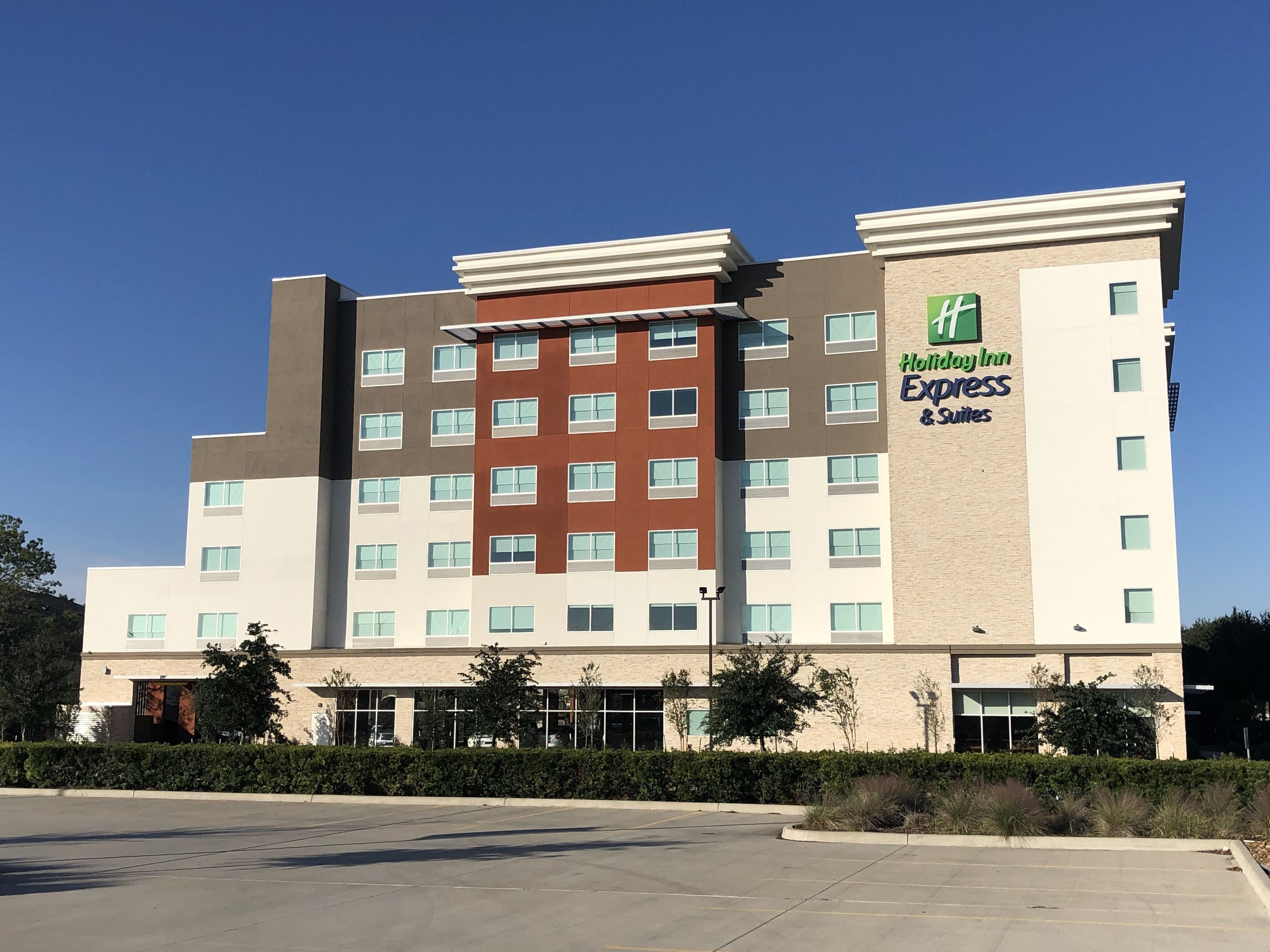 Un bâtiment de la chaîne Holiday Inn Express, doté d’une architecture moderne, avec une façade aux couleurs neutres, un mélange de beige et de brun, de nombreuses fenêtres et un parking situé à l’avant.
