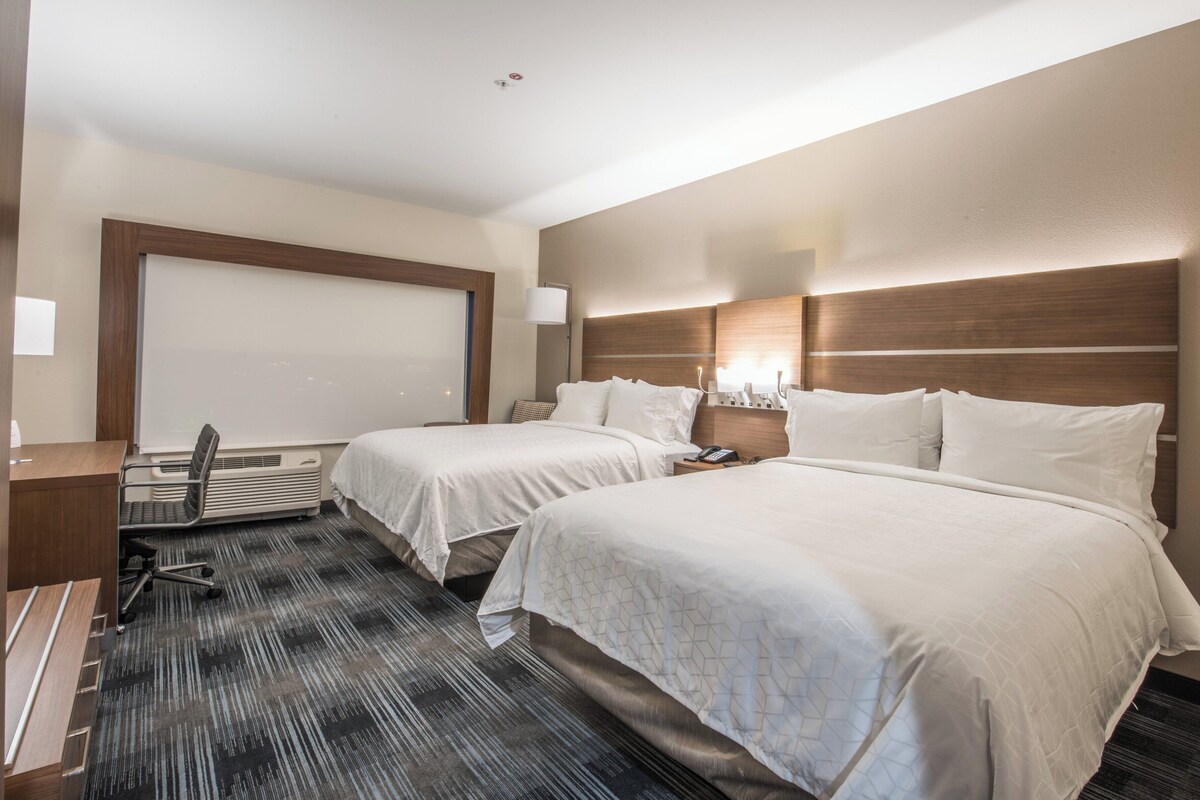 Quarto de hotel com duas camas, uma escrivaninha, uma cadeira, um telefone e uma janela.