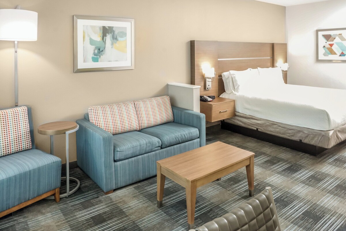 Quarto de hotel com cama, sofá, mesinha, mesa de cabeceira e abajur.