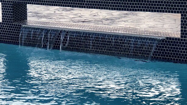 A swimming pool with a tiled edge and a small waterfall feature. - Holiday Inn Express and Suites Houston Westchase - Westheimer by IHG (Houston)