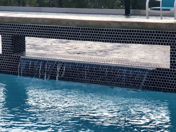 A swimming pool with a tiled edge and a small waterfall feature. - Holiday Inn Express and Suites Houston Westchase - Westheimer by IHG (Houston)