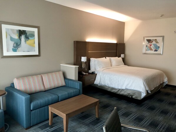 A hotel room with a bed, a blue sofa, a wooden table, and a chair.