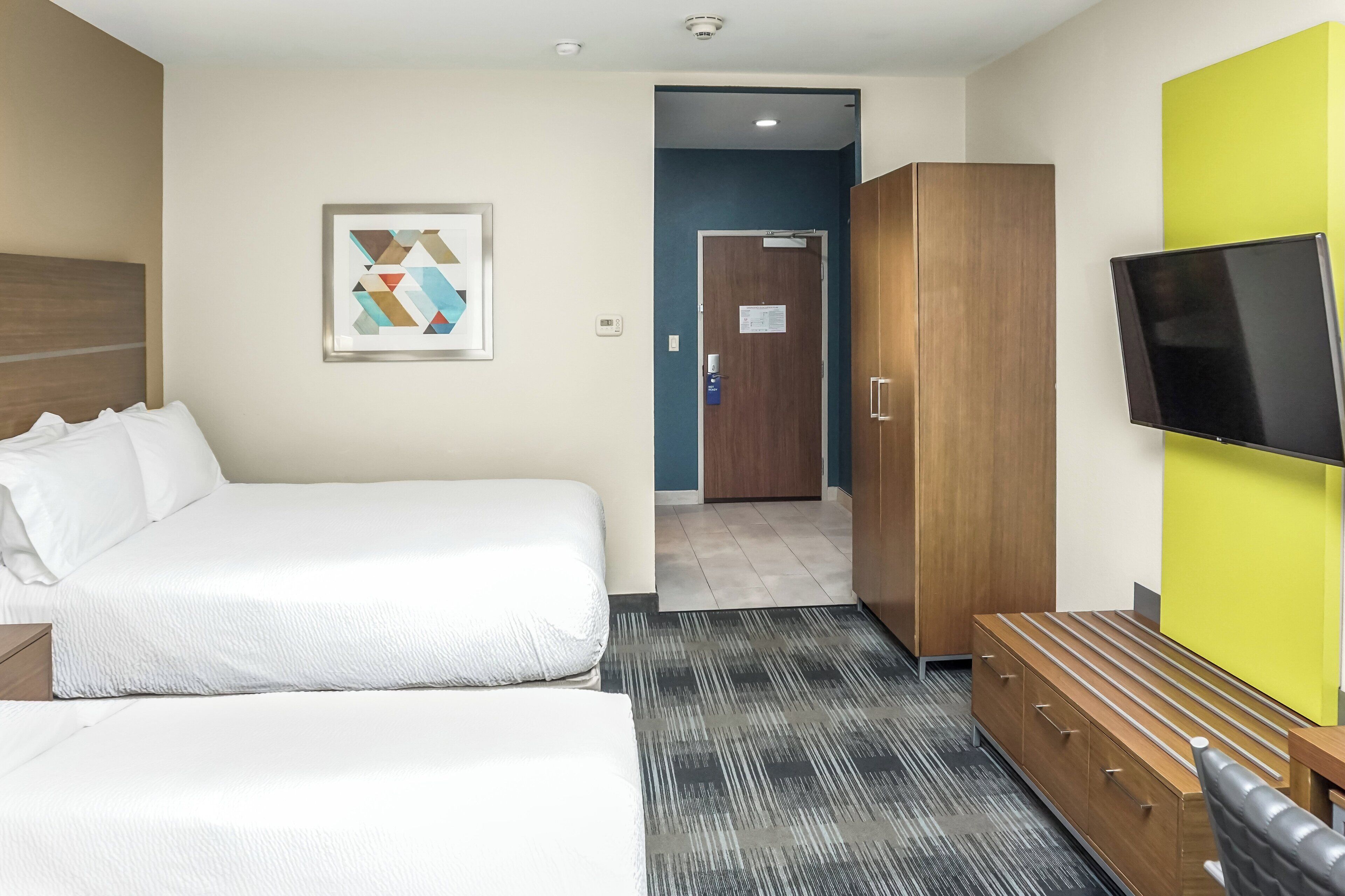 Habitación de hotel con una cama grande, un armario, un televisor de pantalla plana y una obra de arte enmarcada en la pared.