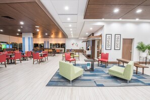 A hotel lobby with multiple seating areas, a reception desk, and a view of the city through large windows.