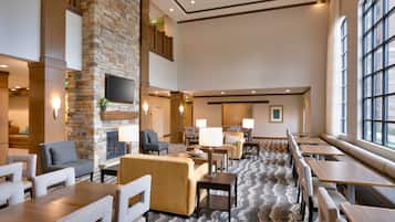 A spacious hotel lobby with a stone fireplace, comfortable seating, and large windows.