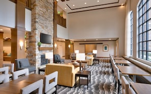 A spacious hotel lobby with a stone fireplace, comfortable seating, and large windows. - Staybridge Suites Gainesville I-75 by IHG (Gainesville)
