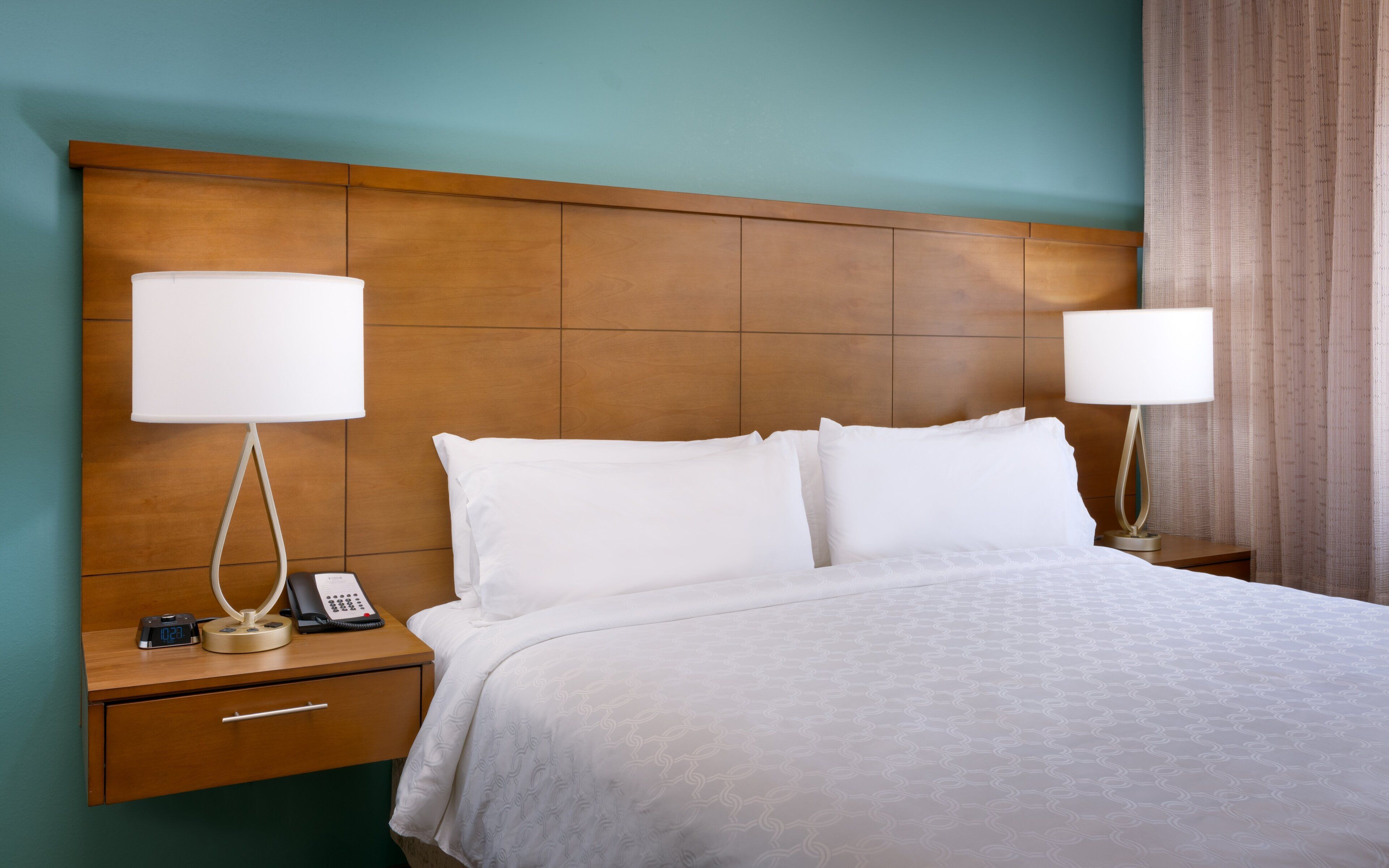 A hotel room with a large bed, two bedside tables with lamps, a nightstand with a phone, and a wooden headboard.