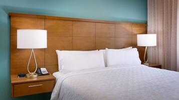 A hotel room with a large bed, two bedside tables with lamps, a nightstand with a phone, and a wooden headboard.