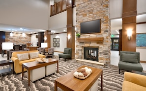 A hotel lobby with a stone fireplace, comfortable seating, a flat-screen TV, and a dining area. - Staybridge Suites Gainesville I-75 by IHG (Gainesville)