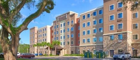 A multi-story hotel with a stone facade, multiple windows, and a parking area with cars.