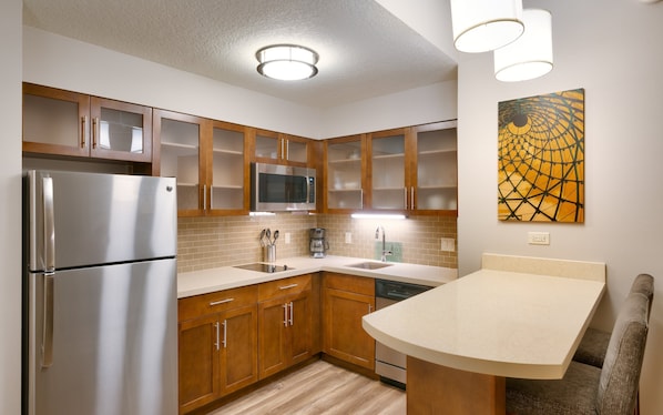 A modern kitchen with wooden cabinets, stainless steel appliances, a microwave, and a coffee maker. - Staybridge Suites Gainesville I-75 by IHG (Gainesville)
