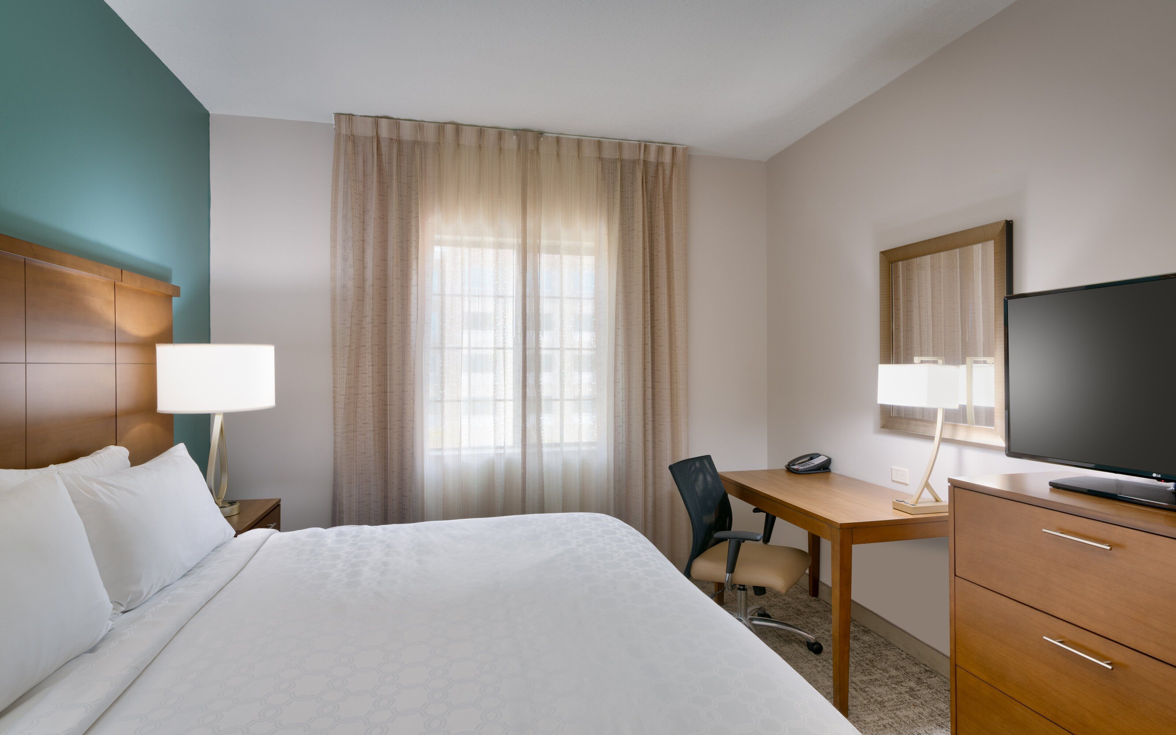 Een hotelkamer met een bed, een bureau, een stoel, een televisie en een telefoon.