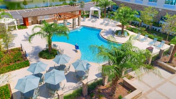 A pool area with lounge chairs and umbrellas, surrounded by palm trees and a building with a stone facade.