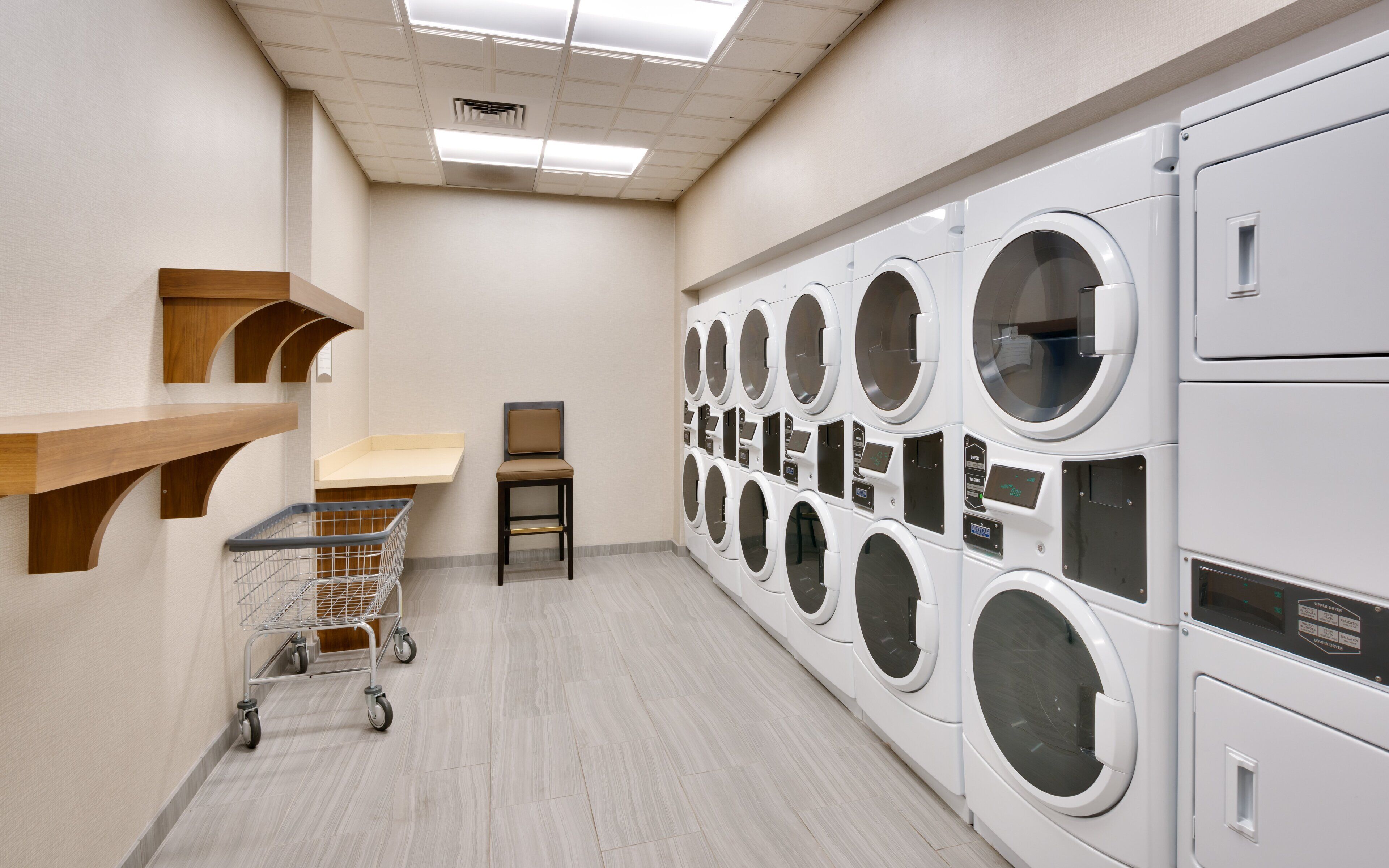A laundry facility with multiple washing machines, a cart, and a chair.