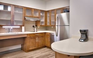 A modern kitchen with wooden cabinets, a stainless steel refrigerator, a coffee maker, and a sink with a faucet. - Staybridge Suites Gainesville I-75 by IHG (Gainesville)