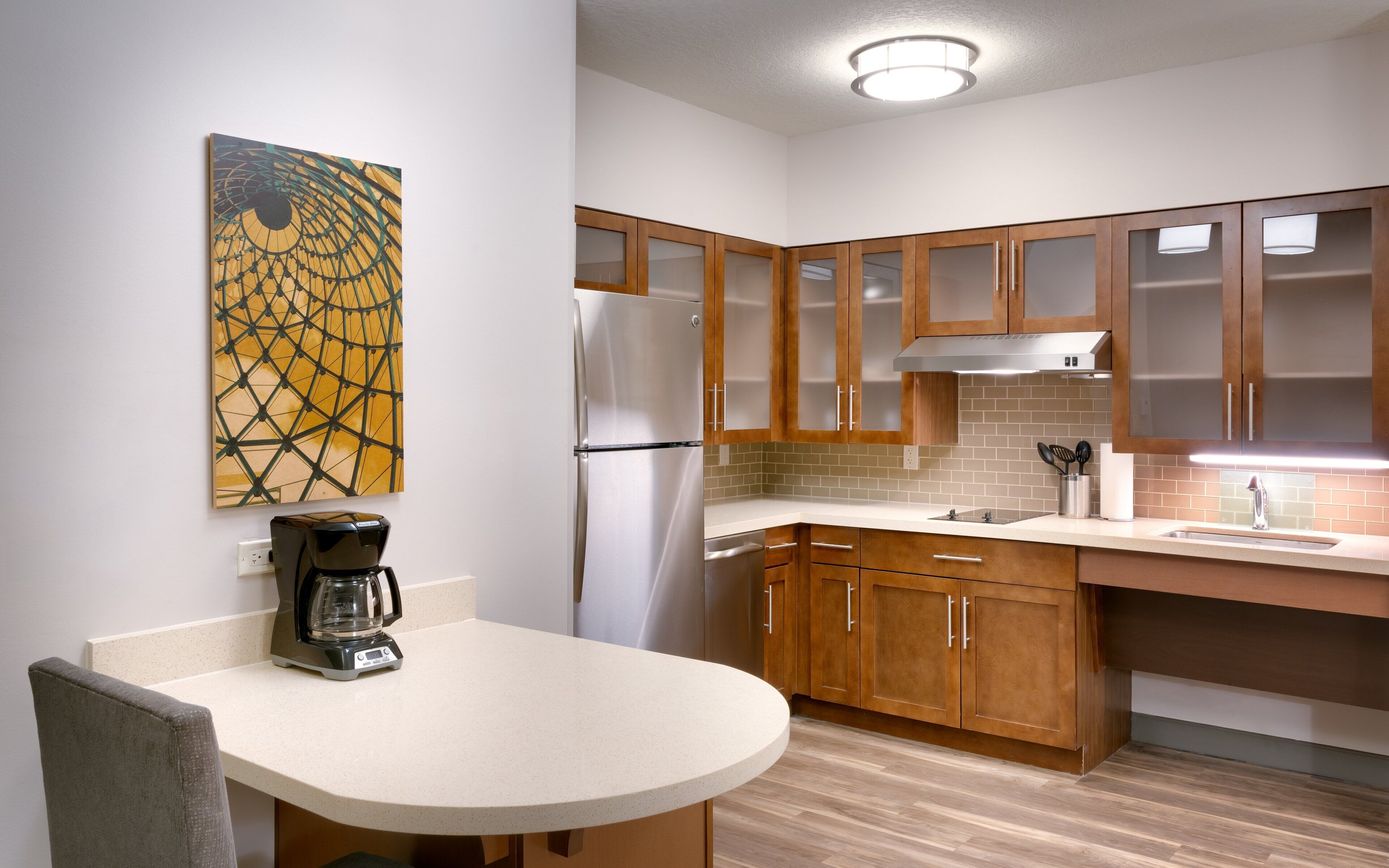 A modern kitchen with wooden cabinets, a stainless steel refrigerator, a coffee maker, and a tiled backsplash.