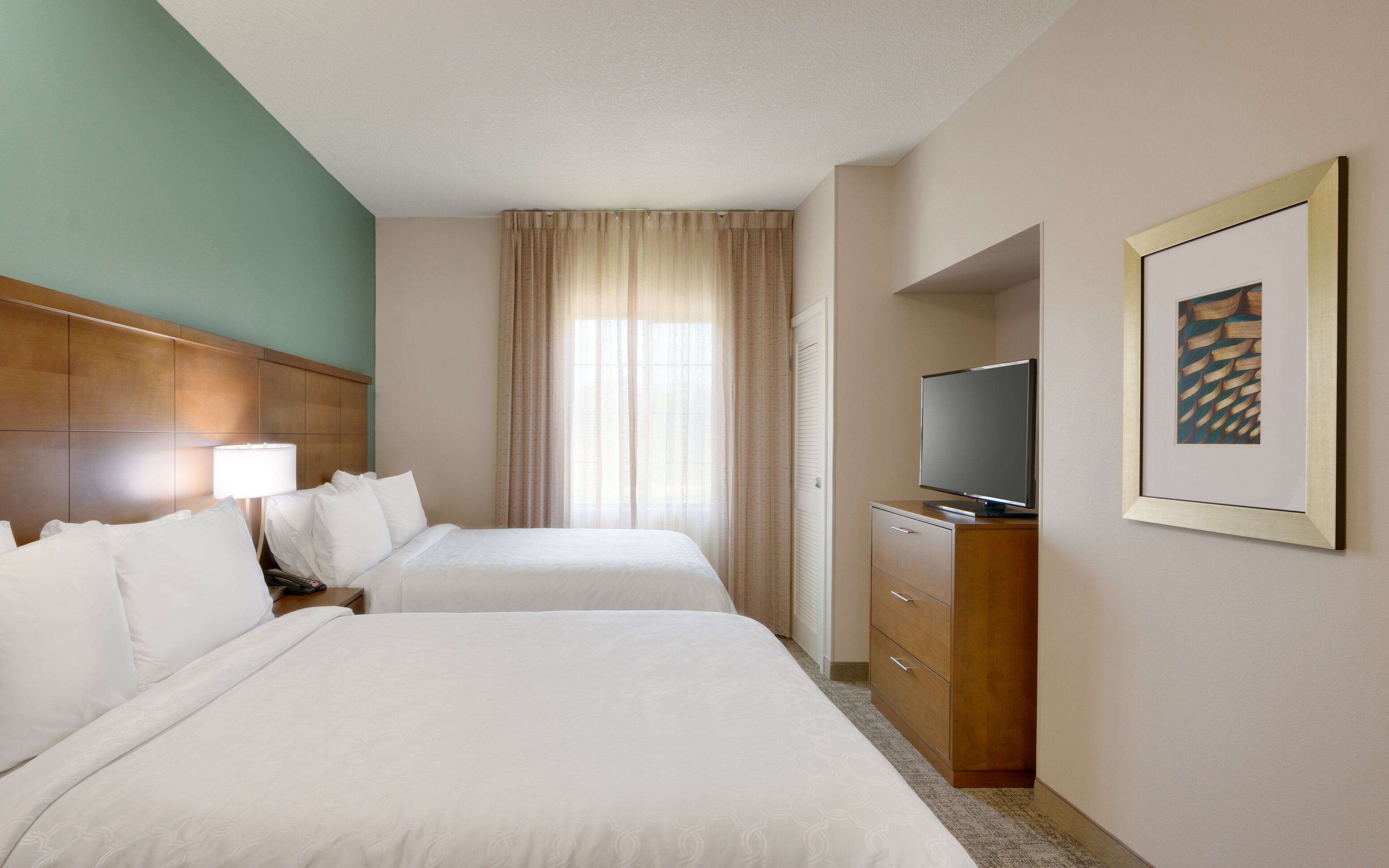 A hotel room with two beds, a TV, a desk, and a framed picture on the wall.
