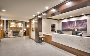 A hotel lobby with a stone fireplace, a reception desk, and a large framed picture of a bridge. - Staybridge Suites Gainesville I-75 by IHG (Gainesville)