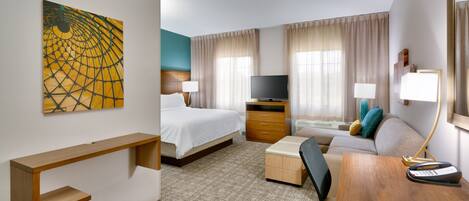 A hotel room with a bed, a desk, a chair, a television, and a painting on the wall.