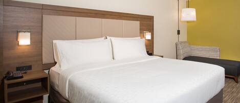 A hotel room with a large bed, bedside tables, a lamp, and a chair.