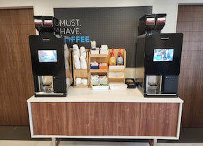 Una estación de café con dos máquinas de café, un cartel que dice "UMUST. HAVE. COFFEE." y diversos artículos relacionados con el café en estantes.