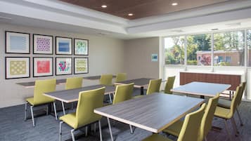 A conference room with tables and chairs, framed artwork on the wall, and a view of trees and a building outside.