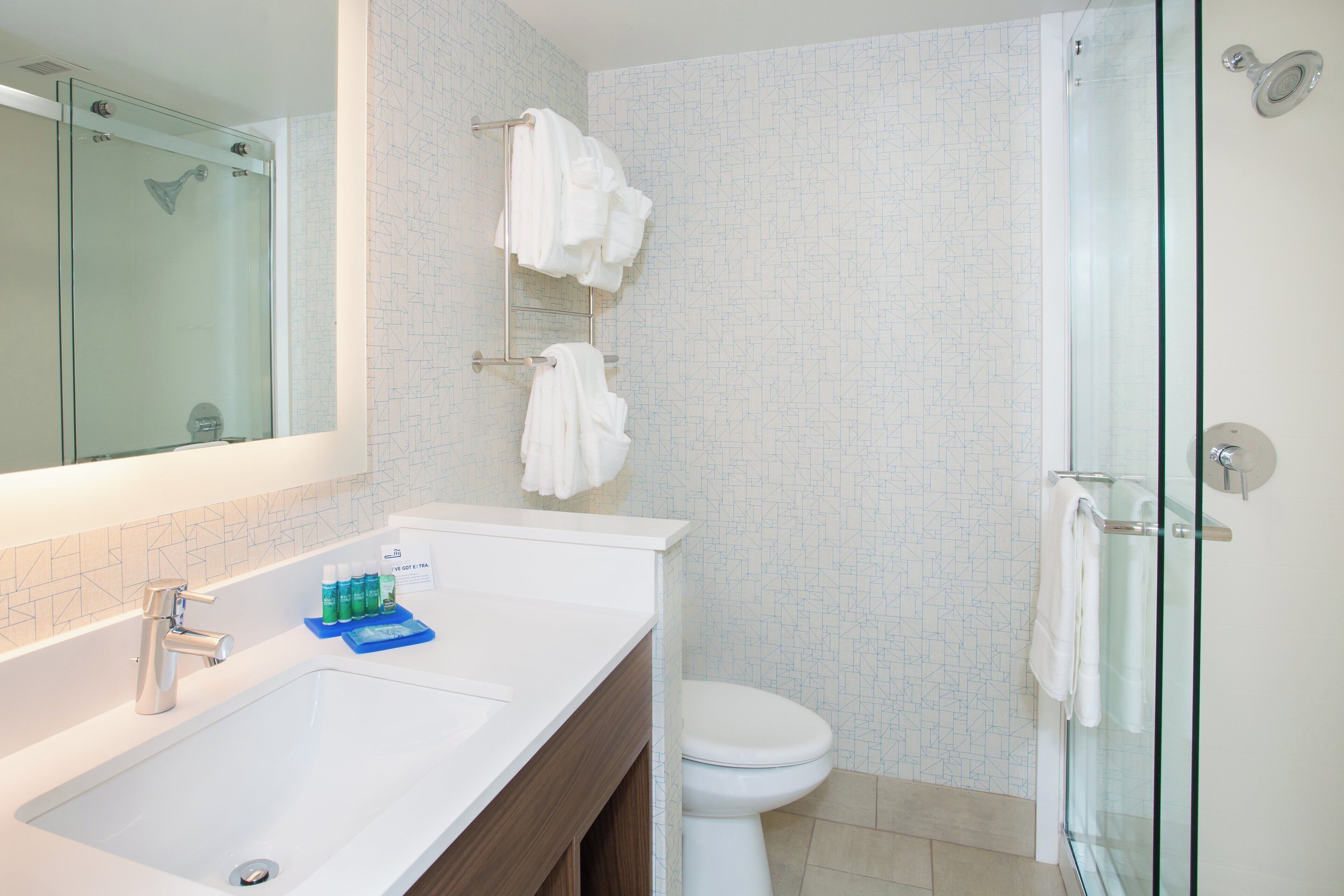 A modern bathroom with a large mirror, a white sink, a toilet, and a glass shower enclosure.