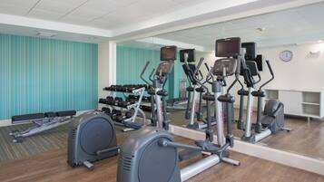 A gym with various exercise equipment, including treadmills, ellipticals, and dumbbells.
