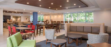 A modern indoor space with seating arrangements, tables, and a view through large windows.