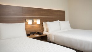 Ein Hotelzimmer mit zwei Betten, einem Holz-Kopfteil, Nachttischlampen, einem Nachttisch und einem Telefon.