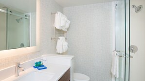 Ein modernes Badezimmer mit Duschkabine aus Glas, einem weißen Waschbecken mit Spiegel und einer Toilette.