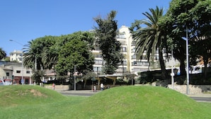 A grassy area with a stone wall and a building with balconies in the background.