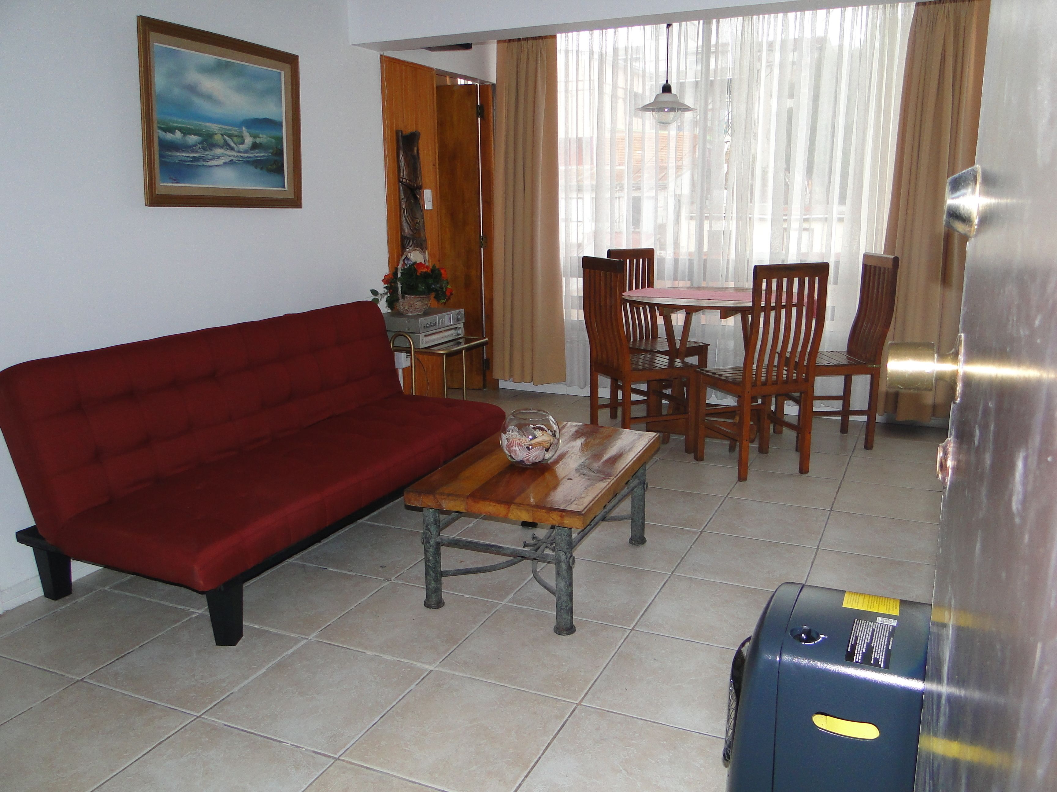 A living room with a red sofa, a wooden coffee table, and a dining area with wooden chairs and a table.