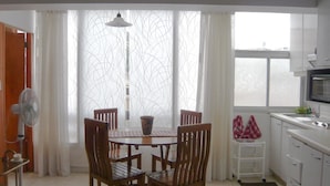 A dining area with a table and chairs, a fan, and a window with curtains.