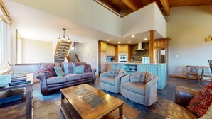 Ein geräumiges Wohnzimmer mit einer Couch, zwei Sesseln, einem Couchtisch und einer Treppe, die in eine obere Etage führt.