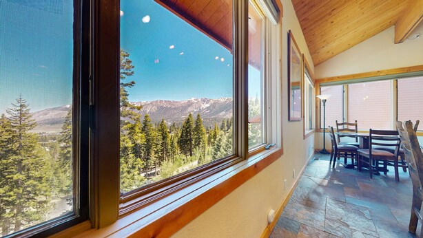 Ein Zimmer mit großen Fenstern und Bergblick, einem Essbereich mit Holmöbeln und einem Steinboden.