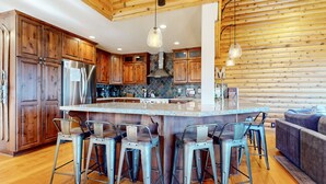 Una cocina con armarios de madera, una isla central con taburetes de bar, un refrigerador de acero inoxidable y una lámpara colgante.