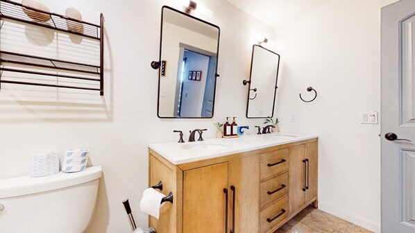 Un baño con inodoro, lavabo de dos grifos, espejo y toallero.