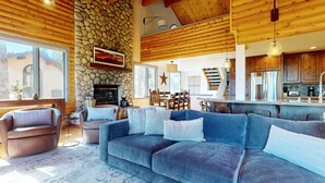 Un salón amplio con chimenea de piedra, techo de madera y un gran sofá con cojines.