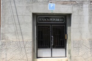 Una entrada de edificio con un letrero que dice "PENSION PEPERILLO" y una señal de estacionamiento arriba.